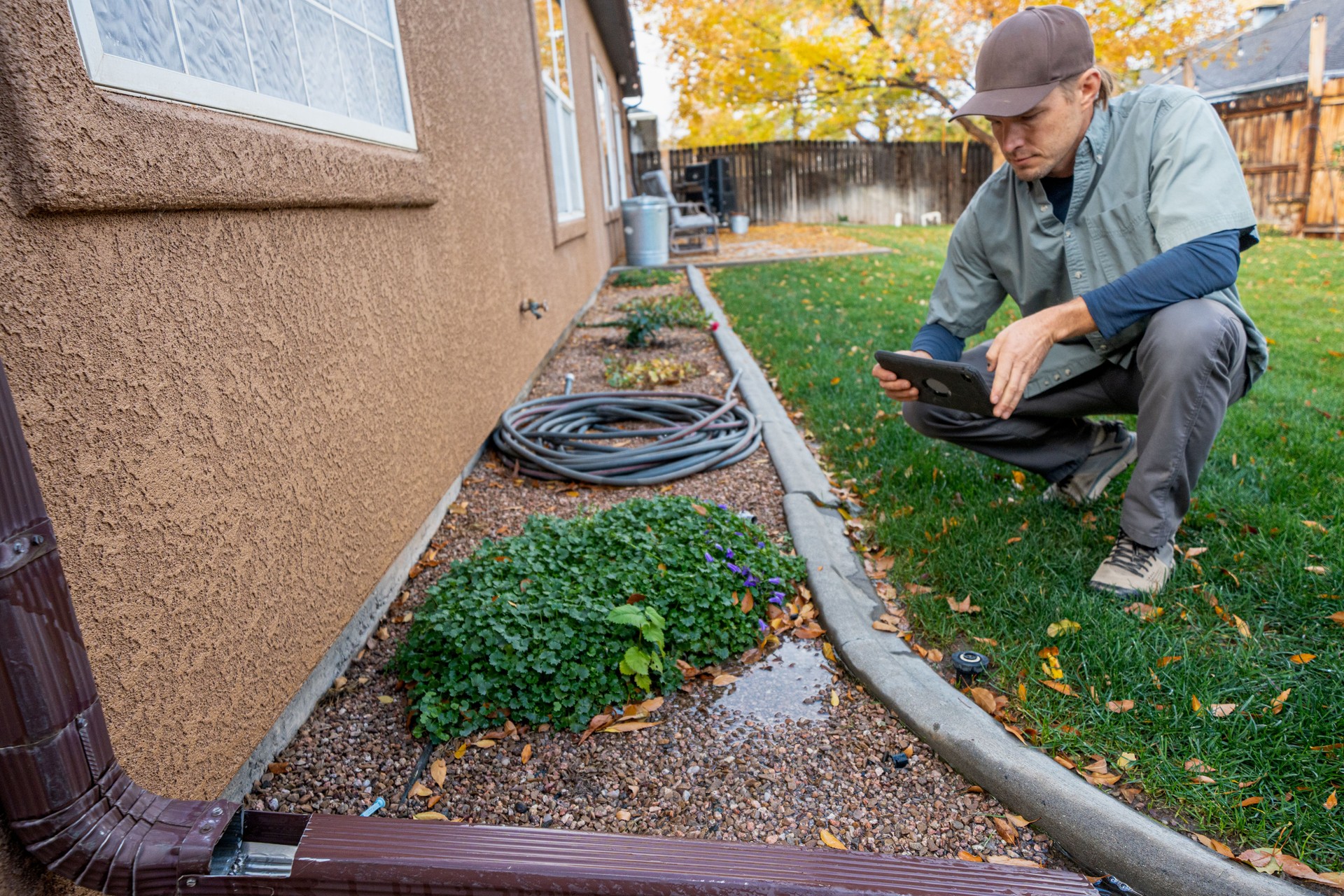 Building Inspector Photographing Leaks and Pooling Water Near a Gutter Downspout in the Back Yard of a Modern Home