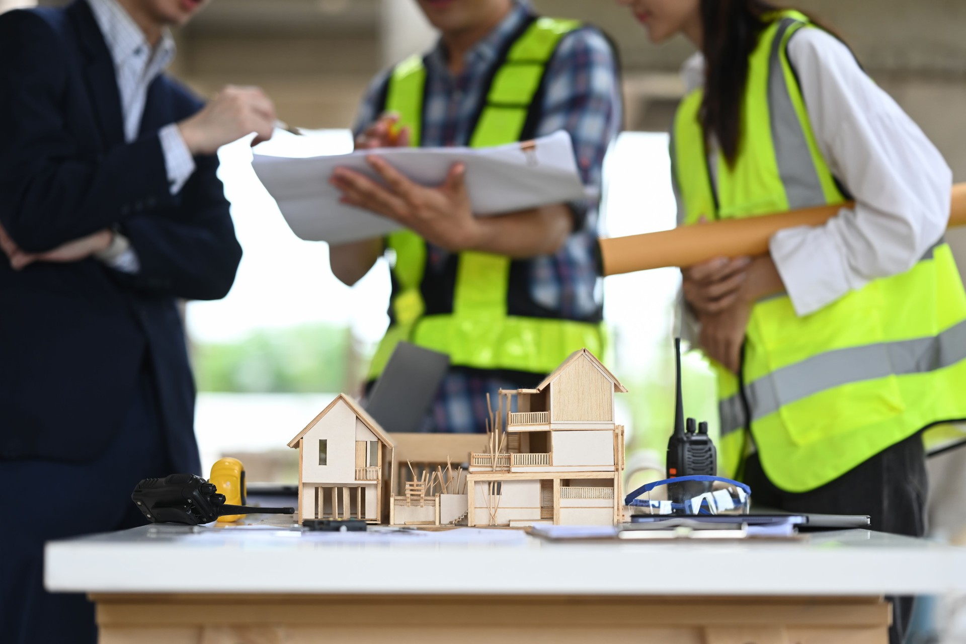 Architectural model of a house with blueprint and tools on table, engineers team working in blurred background.