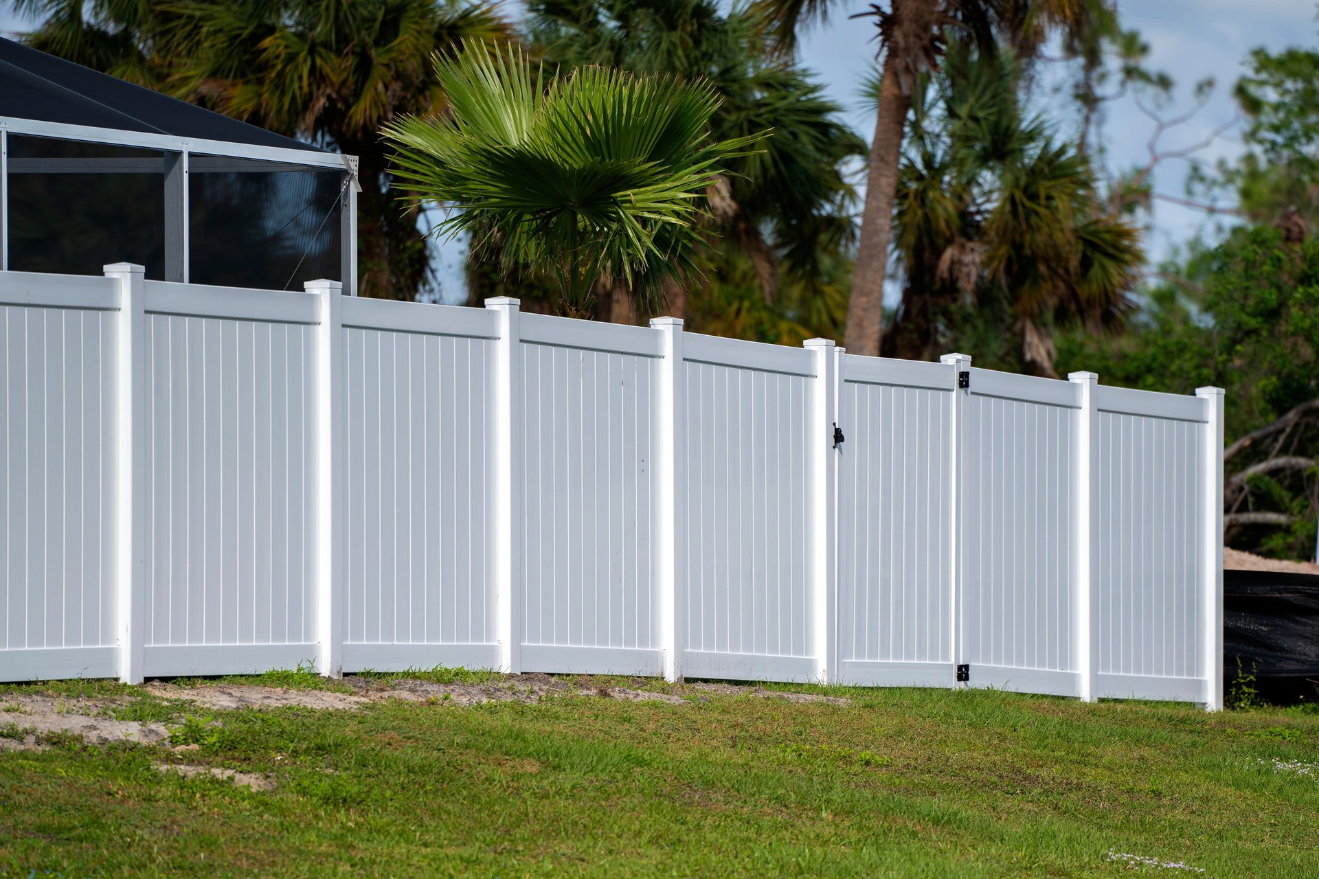 White vinyl picket fence on green lawn surrounding property grounds for backyard protection and privacy